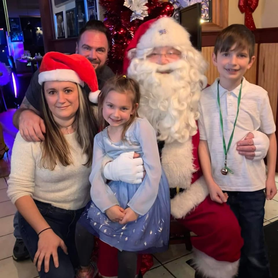 Santa poses with two children and two adults beside a decorated Christmas tree inside a restaurant.