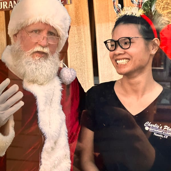 Smiling restaurant staff member wearing glasses and a festive headband poses beside Santa Claus at Charlie’s Place Restaurant and Lounge.