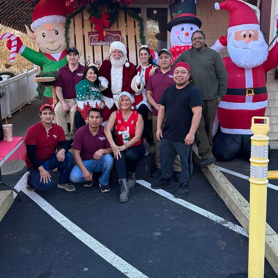 Restaurant staff pose with Santa, snowman, and festive inflatables outside a holiday-decorated restaurant entrance.