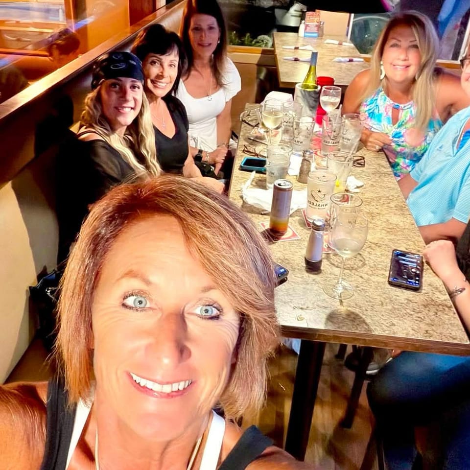 Group of friends smiling for a selfie around a restaurant table with drinks in a warmly lit dining room.