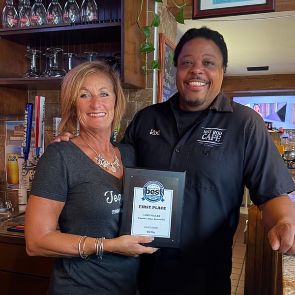 Smiling Hot Rod Cafe bartender and woman pose behind the bar, holding a first-place award plaque.