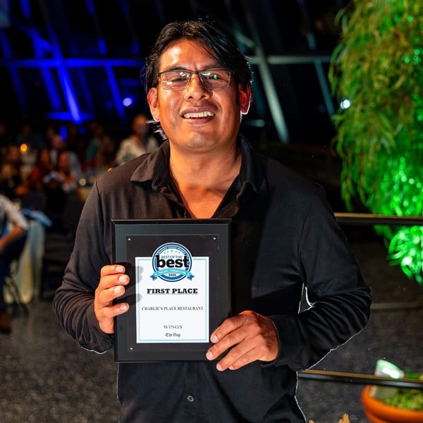 Smiling restaurant staff member holds a first-place award for wings at Charlie’s Place Restaurant in a colorful, dimly lit dining area.
