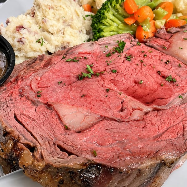 Thick-cut prime rib with mashed potatoes, gravy, and mixed vegetables on a white plate.