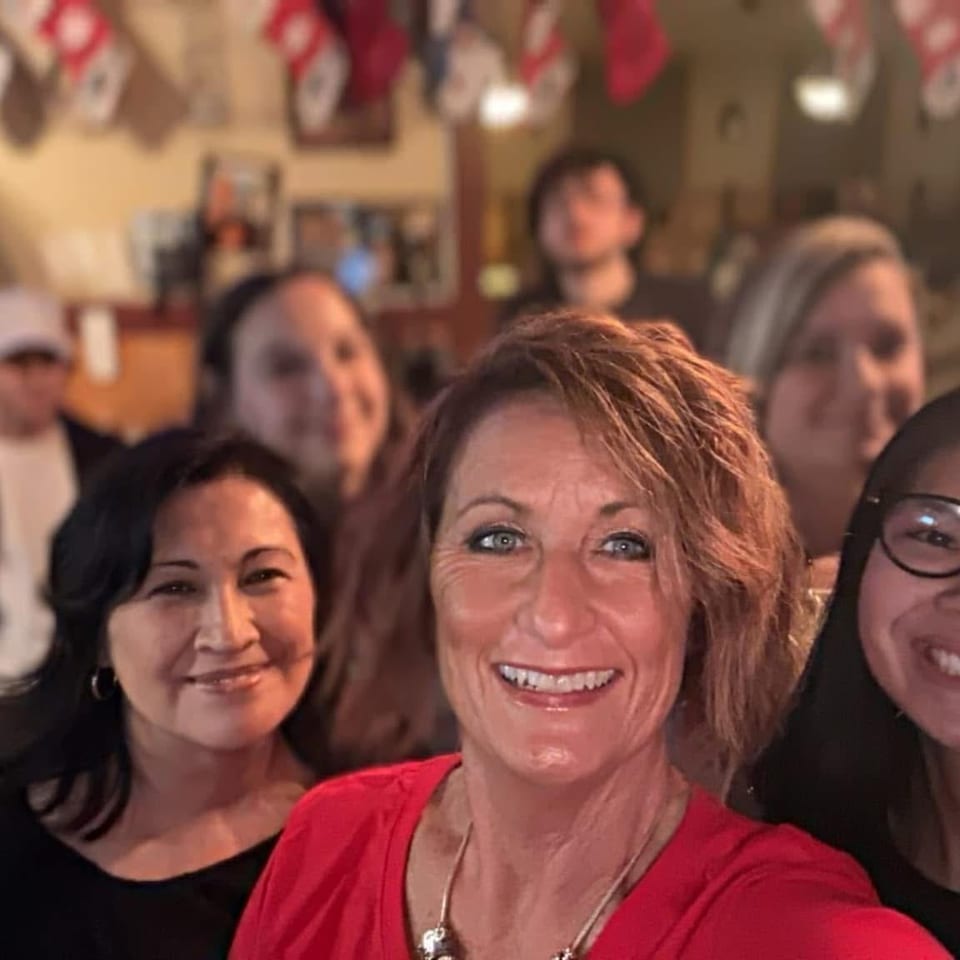 Smiling group poses for a selfie inside a warmly lit restaurant, with festive decorations, tables, and a bar area in the background.