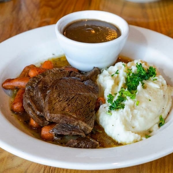 Pot roast with baby carrots, mashed potatoes, and a side of gravy on a white plate.