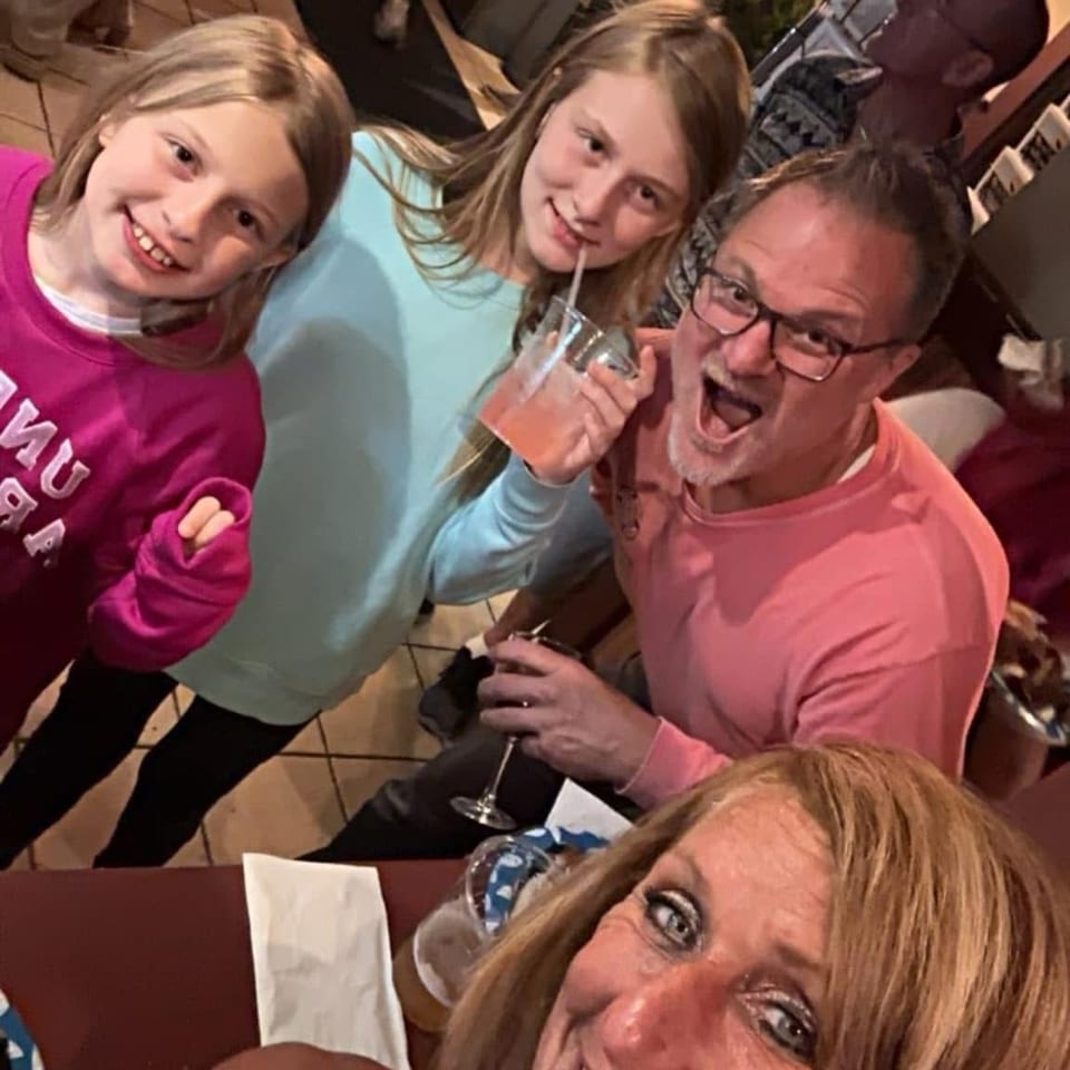 Family and friends smile for a selfie at a lively restaurant table, with one child sipping a pink drink.