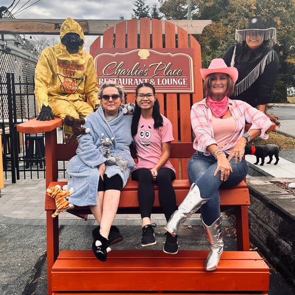 Friends in Halloween costumes pose on a giant orange bench beside the Charles Place Restaurant & Lounge sign.