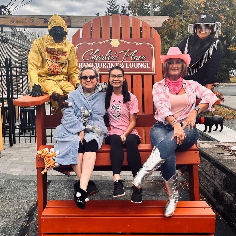 Friends in Halloween costumes pose on a giant orange bench beside the Charles Place Restaurant & Lounge sign.