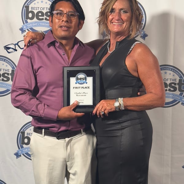 Two people pose with a first-place Charlie’s Place Restaurant award at a Best of the Best Readers’ Choice backdrop.