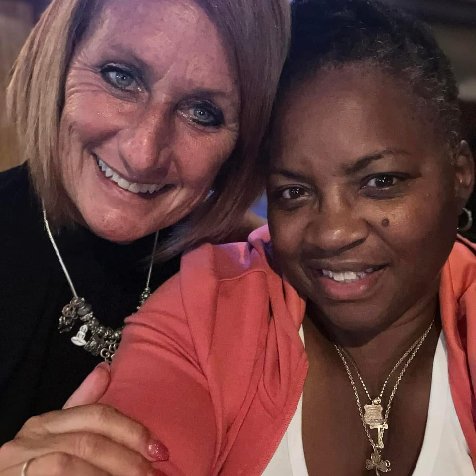 Two smiling women pose closely together for a selfie in a dimly lit restaurant.