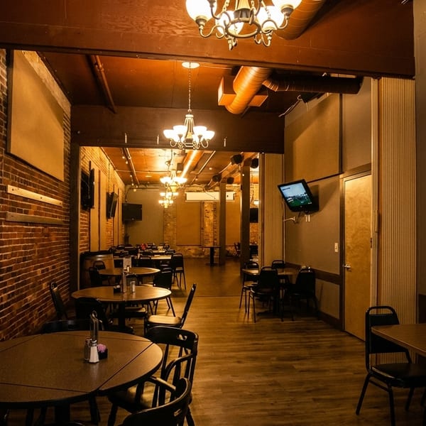 A dimly lit restaurant interior with brick walls, wooden floors, round tables, and a TV showing golf.