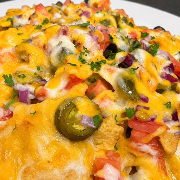 Close-up of cheesy nachos topped with tomatoes, red onions, black olives, jalapeños, and parsley.