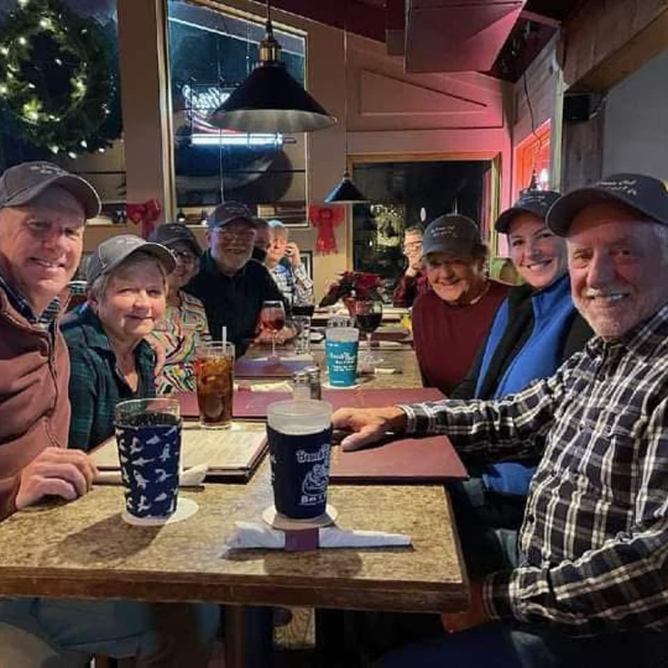 Group of friends smiling around a restaurant table with drinks during a festive evening gathering.