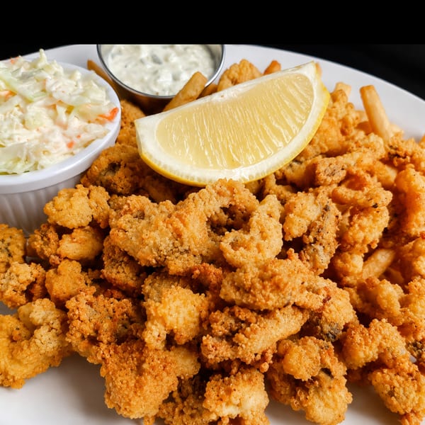 Fried whole belly clams with fries, coleslaw, tartar sauce, and a lemon wedge.