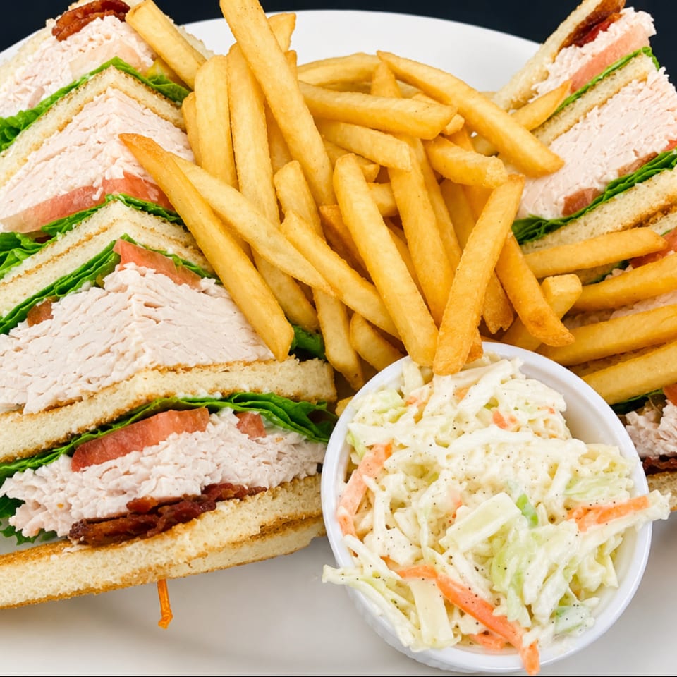 Turkey club sandwich quarters with lettuce, tomato, and bacon served alongside golden fries and creamy coleslaw.