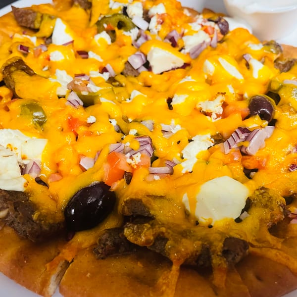 Loaded nachos topped with melted cheddar, seasoned beef, jalapeños, olives, diced tomatoes, onions, and white cheese, served with sour cream.