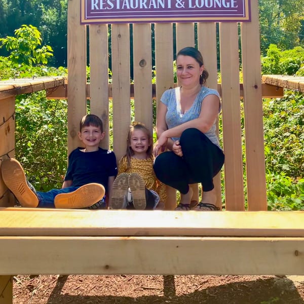 A woman and two children pose on a wooden deck beneath a Charles Place Restaurant & Lounge sign, surrounded by greenery.