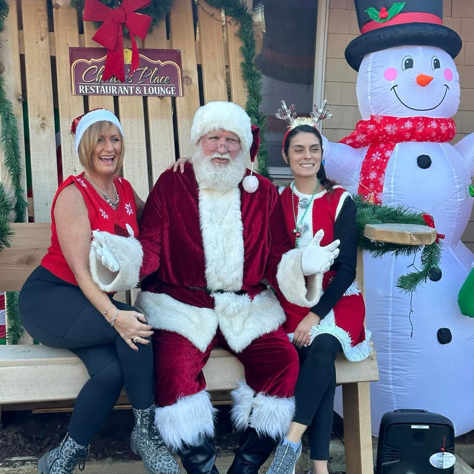 Santa, two women, and an inflatable snowman pose outside Chars Place Restaurant & Lounge amid festive Christmas decorations.