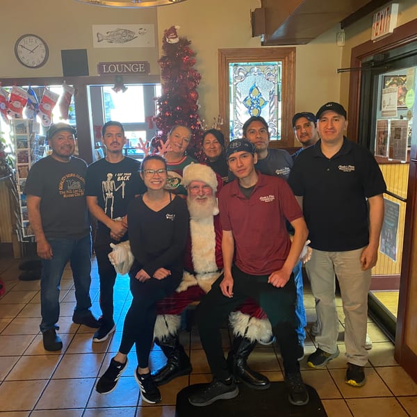Restaurant staff pose with Santa beside a decorated Christmas tree in a warmly decorated lounge.