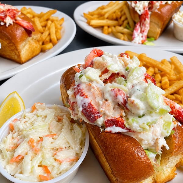 Lobster rolls on toasted buns with fries, coleslaw, and a lemon wedge.