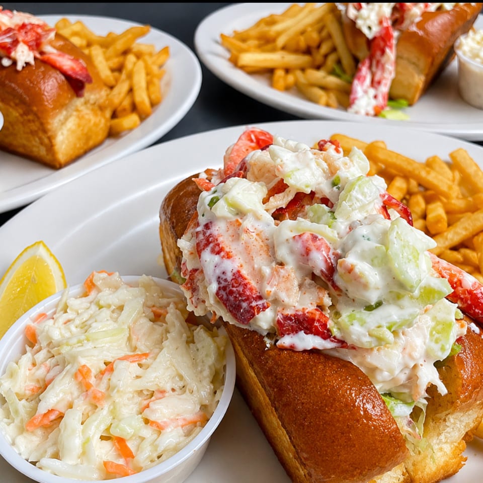 Lobster rolls on toasted buns with fries, coleslaw, and a lemon wedge.