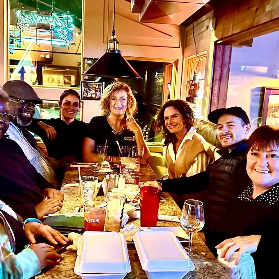 Group of friends smiling together at a restaurant table with drinks and takeout containers.
