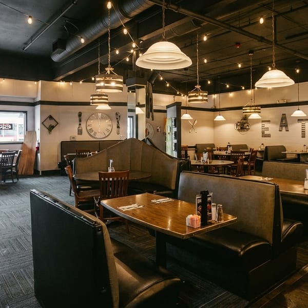 Spacious restaurant interior with booths, tables, string lights, and a large clock on the wall.