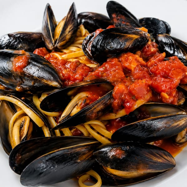 Linguine topped with mussels and chunky tomato sauce on a white plate.