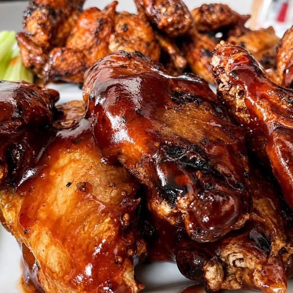 Close-up of glossy barbecue chicken wings with celery sticks on a white plate.